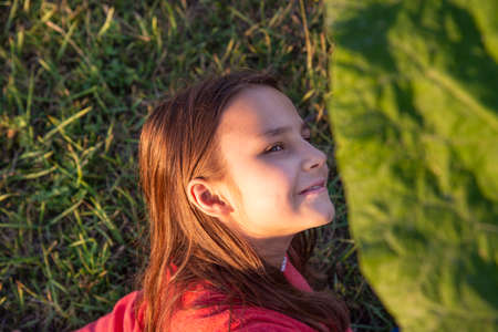 A girl in the Golden hour with a large green burdock leaf on a background of green grassの写真素材