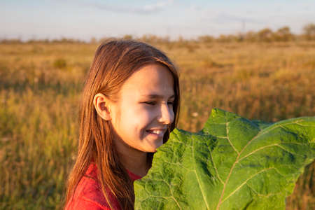 A girl with a large green burdock leaf in a field in the Golden hour