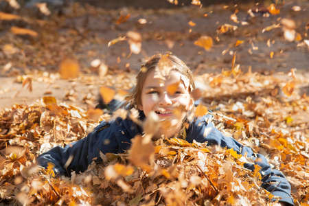 A smiling girl lies in a pile of autumn Golden leaves. In front of the flying autumn leaves