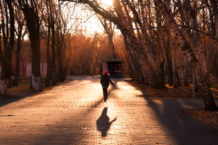 Silhouette of a girl in a red cap running along an empty autumn path in the Park