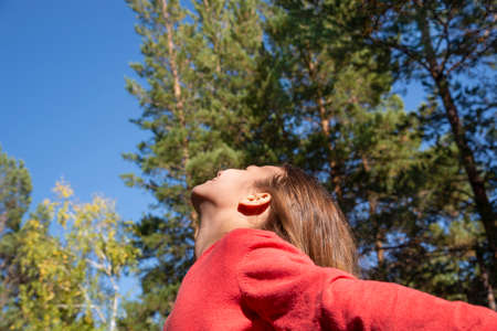 A girl with long hair in a red jacket is spinning against the background of tall trees in the...
