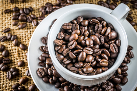 Cup full of coffee beans on the burlap backgroundの写真素材