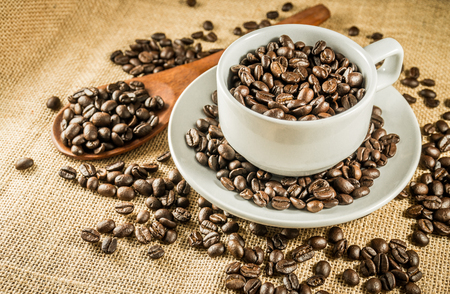 Cup full of coffee beans on the burlap backgroundの写真素材