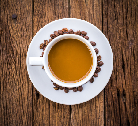 Cup of coffee on a wooden desk with coffee beans, top viewの写真素材