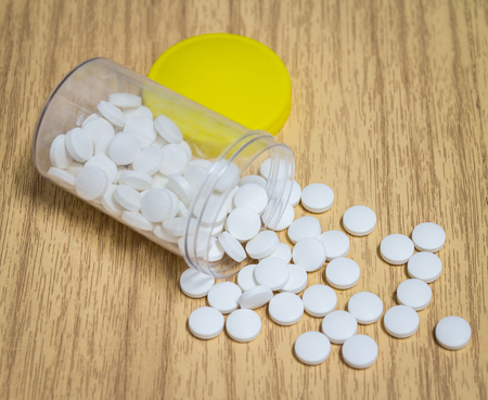 White pill spilling from a prescription medicine bottle on wood deskの写真素材