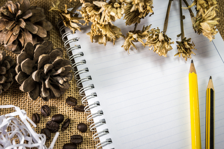 Pencil on notebook with dry flower on burlap backgroundの写真素材