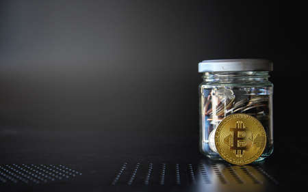 Gold bitcoin and money coin in glass jar on black background. Crypto currency and finance concept.の写真素材