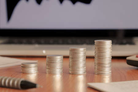 Stack of money coin with laptop computer open trading graph in the background, Business and Financial concept.の写真素材