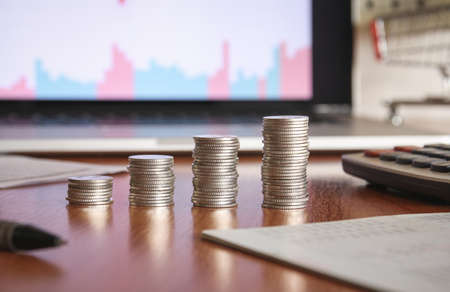 Stack of money coin with laptop computer open trading graph in the background, Business and Financial concept.の写真素材