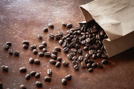 Roasted coffee beans spilling from brown paper bag with selective focus on old brown backgroundの写真素材