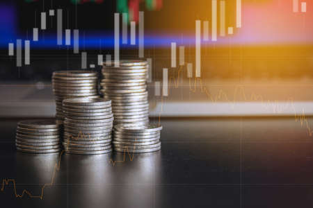Stack of money coin and laptop computer with trading graph, financial investment concept with blue filter can be use as backgroundの写真素材