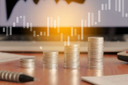 Stack of money coin and laptop computer with trading graph, financial investment concept with blue...