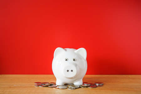 White Piggy bank and coin on wooden desk with red backgroundの写真素材