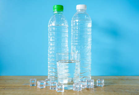 Refreshing natural mineral water in plastic bottle with transparent glass and ice cubes on wooden desk with blue backgroundの写真素材
