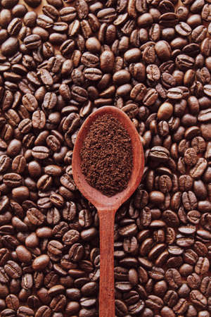 Ground coffee in wooden spoon with coffee beans backgroundの写真素材
