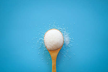 Top view of white sugar in wooden spoon on blue backgroundの写真素材