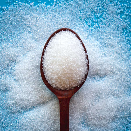 Top view of white sugar in wooden spoon on blue backgroundの写真素材
