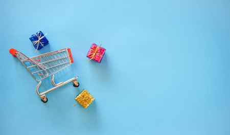 Shopping cart with gifts on blue background. Top view with copy spaceの写真素材