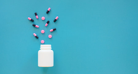 Pills spilling out of pill bottle on blue background. Copy spaceの写真素材
