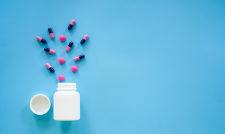 Pills spilling out of pill bottle on blue background with copy spaceの写真素材