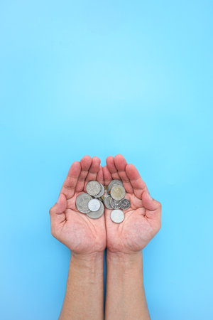 Coins in female hands on blue background. Saving money concept.の写真素材