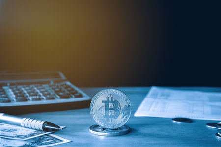 Bitcoin cryptocurrency coin on table with dollar banknote, calculator and pen.の写真素材