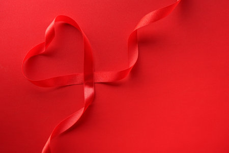 Red ribbon in shape of heart on color background. Valentine's day celebrationの写真素材