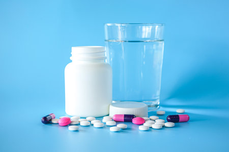 Pills and glass of water on blue background. Focus on foreground.の写真素材