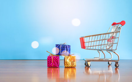 Shopping cart with gift boxes on wooden table and blue background.の写真素材