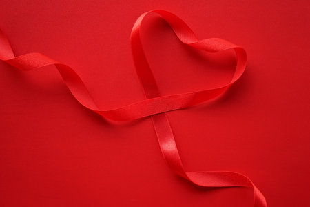 Red heart shaped ribbon on red background. Valentine's day concept.の写真素材