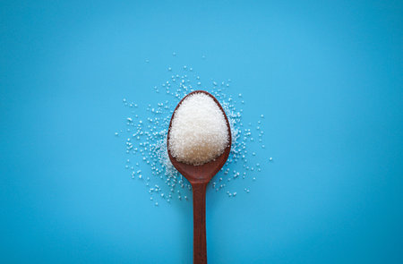 Sugar in a wooden spoon on a blue background, top viewの写真素材