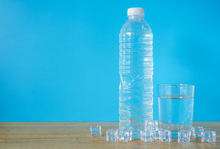 Bottle of water and ice cubes on wooden table. Blue backgroundの写真素材
