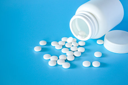 White pills spilling out of pill bottle on blue background. Focus on foreground, soft bokeh. Pharmacy drugstore concept.の写真素材