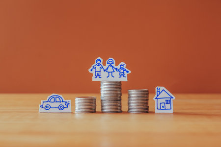Coins stack with family, house and car icon on wooden table and brown backgroundの写真素材