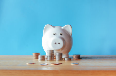 Piggy bank with coins on wooden table and blue background.の写真素材