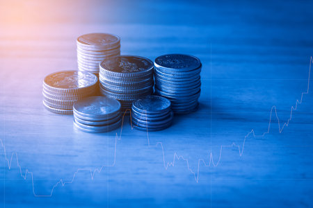 Coins stack on wooden table with financial graph background, business and finance concept idea.の写真素材
