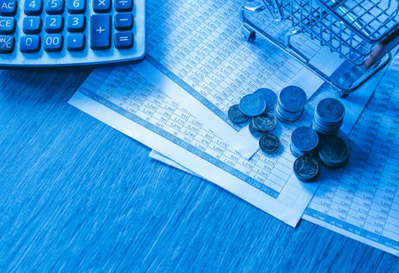 Shopping cart, coins and calculator on the table in blue toneの写真素材