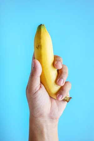 Hand holding a banana isolated on blue background with copy space for textの写真素材