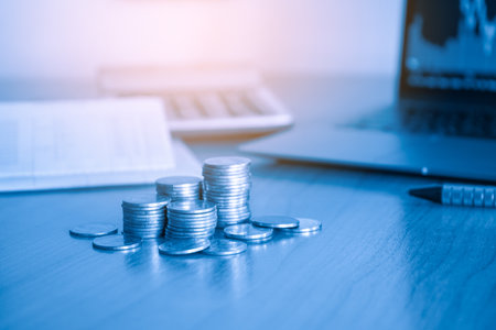 Coins stacked on the table with laptop and calculator on the background.の写真素材