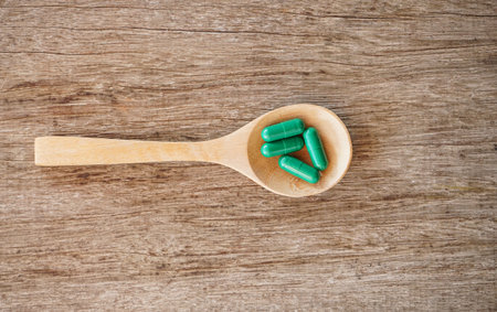 Green capsule pill in wooden spoon on wood background, Health care and medical conceptの写真素材