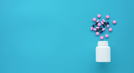 Pills spilling out of pill bottle on blue background with copy spaceの写真素材