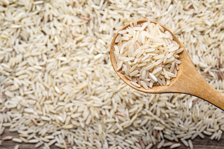 Raw rice in wooden spoon on brown rice background. Top view.の写真素材