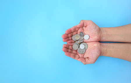 Coins in female hands on a blue background. The concept of saving money.の写真素材