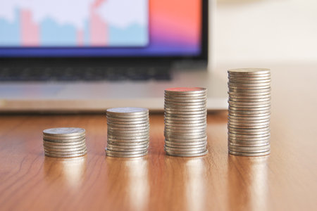 Stacks of coins with laptop on wooden table, business and finance conceptの写真素材
