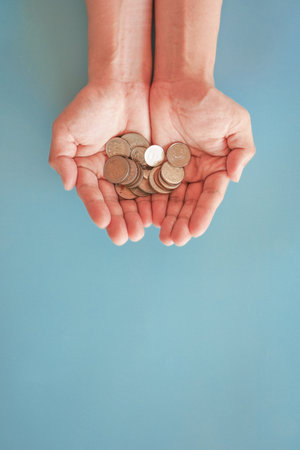Coins in female hands on a blue background. Concept of saving money.の写真素材