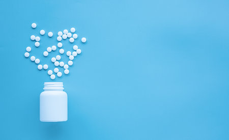 Pills spilling out of pill bottle on blue background with copy spaceの写真素材