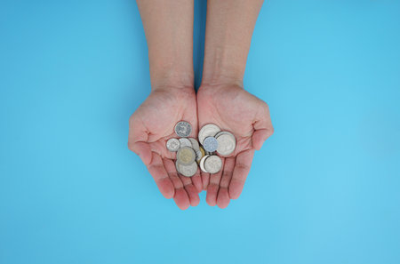 Female hands holding coins on a blue background. Save money concept.