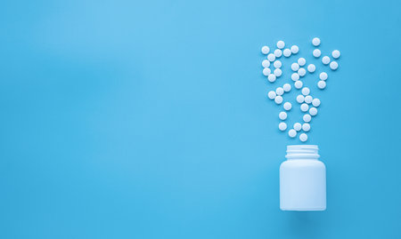 Pills spilling out of pill bottle on blue background with copy spaceの写真素材