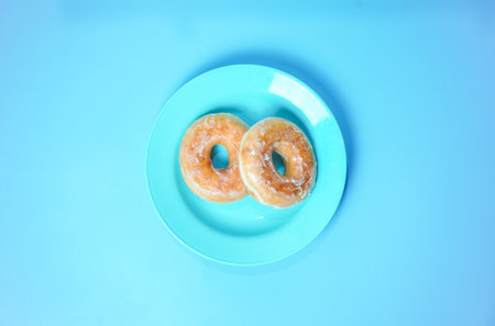 Two donuts on a blue plate on a blue background, top viewの写真素材