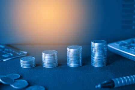 Stacks of coins with credit card and calculator on dark background.